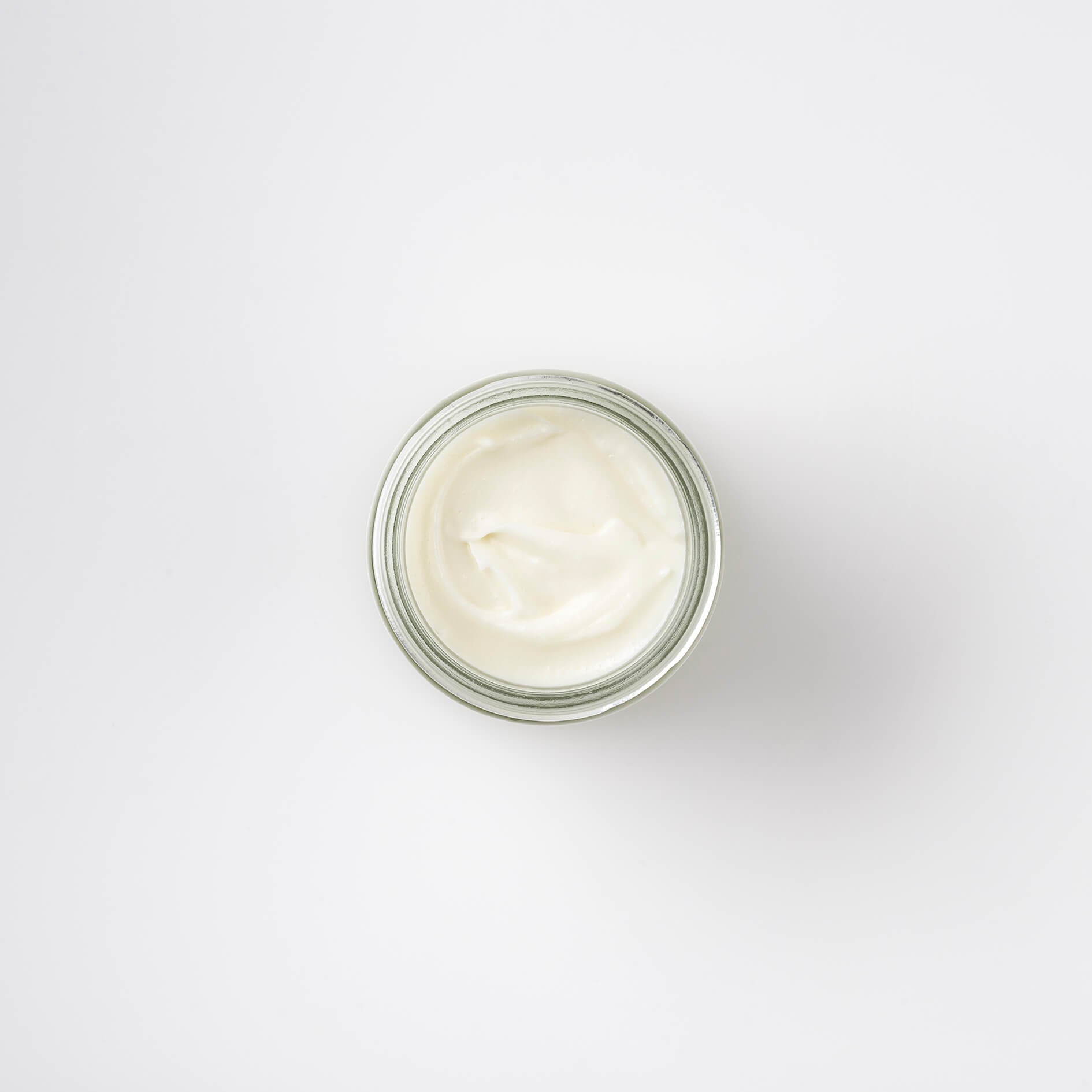 photo of the top view of an off white face cream in a 60ml clear glass jar, shows the smooth, creamy texture of the product.